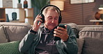Senior man, phone and headphones on sofa, relax and streaming with audio subscription in living room. Elderly person, smartphone and listen to music on mobile app, radio and happy in retirement home