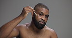 Face, skincare and black man with beauty serum for collagen treatment or dermatology. Portrait, dropper and apply facial cosmetics for hydration or glow with hyaluronic acid on gray studio background