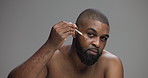 Face, skincare and man with serum for cosmetics, natural beauty or dermatology. African person, dropper and apply facial treatment for hydration or glow with hyaluronic acid on gray studio background