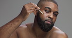 Face, skincare and man with serum for treatment, essential oil or dermatology. African person, dropper and apply facial cosmetics for hydration or glow with hyaluronic acid on gray studio background