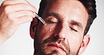 Man, face and oil with dropper in studio for vitamin c, collagen or dermatology on a white background. Portrait, male person or model applying hyaluronic acid with serum pipette for facial treatment