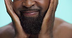 Hands, moisturizing and man with beard, studio and grooming with cosmetics in morning, smile or confident. Blue background, fresh shave and black person with routine for self care or facial treatment