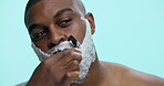 Razor, shaving and man with cream, beard and routine for hygiene in studio and facial treatment. Blue background, grooming and black person with product for hair removal, brush and mockup space