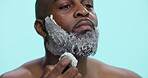 Morning, shaving and man with cream, beard and routine for hygiene in studio and facial treatment. Blue background, grooming and black person with product for hair removal, brush and mockup space