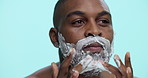Studio, shaving and man with foam, beard and routine for hygiene in morning and facial treatment. Blue background, grooming and black person with product for hair removal, space and cream on face