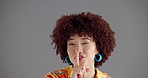 Happy woman, face and secret with afro in studio for fashion or style on a gray background. Portrait, female person or model with smile or finger on lips for gossip, confidential or hush on space