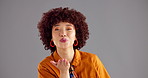 Happy woman, face and blowing with kiss in studio for love, affection or emotion on a gray background. Portrait, female person or model with smile or romantic gesture for flirt, care or distance