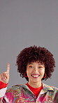 Happy woman, face and pointing up with fashion for retro party, style or sale on a gray studio background. Portrait, female person or model with smile, afro or gesture for advertising on mockup space