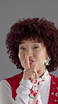 Face, wink and woman with finger on lips, smile and noise with expression on gray studio background. Portrait, happy person and model with hand gesture, privacy and gossip with mystery and secret