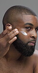 Studio, moisturizing and man with cream, skincare and self care with facial treatment, shine and morning. Gray background, cosmetics and black person with lotion for glow, dermatology and grooming