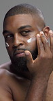 Studio, grooming and man with cream, skincare and self care with facial treatment, shine and morning. Gray background, routine and black person with lotion for glow, dermatology or cosmetics for face