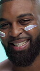 Black man, happy and lotion on face in studio for skincare, cosmetics or moisturizer on blue background. Smile, portrait and male person with cream, sunscreen or facial treatment for dermatology