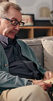 Senior man, reading book and couch in home, relax and knowledge in retirement with glasses in living room. Elderly person, novel and literature on sofa with poetry, language and lounge at apartment