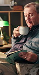 Elderly man, reading book and coffee on sofa in home, relax or blow drink with biology for life extension research. Senior person, novel or study science for anti aging, tea cup or knowledge on couch