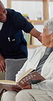 Caregiver, checkup and senior woman with book for healthcare, nursing support and retirement home. Man, discussion and elderly person for reading novel, weekend hobby and assisted living at homecare
