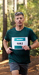 Marathon, face and man with running in woods for endurance challenge, sports event or energy. Runner, mature person and workout for cardio exercise, competition performance and pace training outdoor