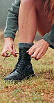 Woman, hands and tying shoes for hiking preparation, safety or trekking adventure on grass field. Closeup, female person or hiker getting ready with boots, tie or laces for journey or walk in nature