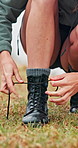 Woman, hands and tie shoes for hiking preparation, safety or trekking adventure on grass field. Closeup, female person or hiker getting ready with boots or tying laces for journey or walk in nature