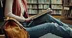 Woman, hands and reading with book in library on floor for education, learning or knowledge. Closeup, female person or student with novel or textbook for story, literature or studying by bookshelf