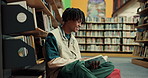Happy man, student and reading with book in library on floor for education, learning or knowledge. Male person, learner or sitting with novel or textbook for literature or studying by bookshelf