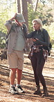 Elderly couple, hiking and phone in woods with search for direction, point and confused on adventure. People, smartphone and mobile app in forest for map, location and lost with talking in Portugal