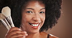 Makeup, brushes and face of black woman by studio background with skincare, beauty or facial routine. Happy, confident and portrait of African female person with cosmetic products for grooming.