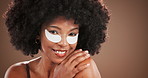 Skincare, face and woman with under eye patches in studio for dark circles, beauty or hydration. Self care, african person and cosmetics product for anti aging treatment and happy on brown background