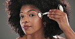 Health, facial roller and face of black woman in studio for natural, beauty or lymphatic drainage. Dermatology, portrait and female person with tool for blood circulation skincare by gray background.