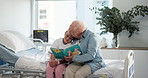 Hospital, book and grandmother reading with child for bonding, support or family time together. Happy, care and senior woman with girl kid for enjoying story, novel or literature in clinic room.