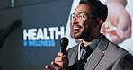 Speaker, conference and man with microphone on stage for health and wellness by screen. Male leader, convention or seminar for training or education, healthcare and medical innovation at event