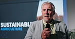 Mature, businessman and presentation at seminar for sustainable agriculture or economic growth. Man, executive or speaker talking with mic or projector screen for environmental production or change