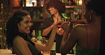Bartender, women and friends toast at a club for fun, cocktail or happy hour at counter. Man, mixologist and people with alcohol beverage at bar or pub for cheers, social event and party on night out