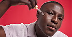 Face, black man and serum for skincare in studio for beauty, hydration and collagen treatment. Portrait, person and smile with pipette for facial oil, dermatology glow and wellness on red background