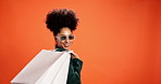 Shopping bag, sunglass and woman in studio happy for bargain, retail sale and discount. Customer, fashion and portrait of person with package for products, cosmetics and style on orange background