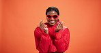 Studio, face and woman with sunglasses, fashion and smile with finger heart, trendy or mockup space. Orange background, happy and black person with stylish outfit, confident and gesture for clothes