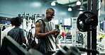 Gym, fitness and man with smile for smartphone, wellness and exercise with barbell for bodybuilding. Texting, online and person with mobile for chat in health club, bodybuilder and workout for muscle