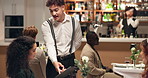 Waiter, customers and women in restaurant, talking and order for food, culinary cuisine and dinner. People, employee or friends with conversation, fine dining and service with hospitality or decision