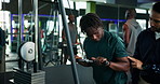 Man, fitness and instructor with demonstration on cable pulley machine for arm exercise or workout. Male people, coach and helping customer with training technique for triceps, reps or tips at gym