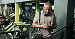 Fitness, phone and black man in gym with networking, communication or chatting on mobile app. Walking, cellphone and African athlete checking workout, exercise or training progress in sports center.