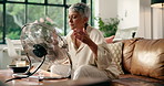 Senior woman, electric fan and cool down in home for hyperthermia and heat. Hot weather, propeller and person in living room for fresh air, ventilation or wind in summer for menopause in retirement