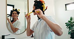 Woman, happy and hair curlers in mirror of bathroom for heatless styling, getting ready and beauty. Reflection, person and haircare in home for self care maintenance, grooming and pinup curls routine