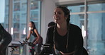 Woman, bike and spin class at gym with smile, strobe lights and coach with motivation for fitness. Person, happy and talk with cycling, workout and training for challenge with group at exercise club