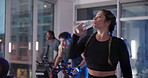 Athlete, woman and drink water on stationary bike at gym for rest, hydration and thirsty from exercise. Person, breathe and machine for refreshing liquid, intense workout or break of cycling recovery