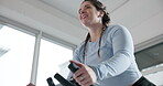 Below, woman and stationary bike for fitness at gym for exercise, cardio training and lose weight. Smile, female person and cycling on machine, endurance workout and intense performance for wellness