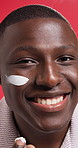 Black man, lotion and skincare with face cream for facial treatment on a red studio background. Male person, African model or moisturizer with smile in joy for anti aging, SPF or skin protection