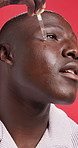 Black man, oil and dropper with serum for facial treatment on a red studio background. Male person, African model or face with pipette or hyaluronic acid for anti aging, collagen or vitamin skincare