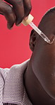 Black man, oil and dropper with serum for skincare or facial treatment on a red studio background. Male person, African model or face with pipette for anti aging, collagen or vitamin skin moisturizer