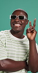 Face, peace sign and black man in studio, fashion and sunglasses on green background. Portrait, African person and happy model with hand gesture, shades and funny with stylish clothes and pride