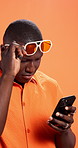 Surprise, smartphone and black man in studio, glasses and notification on orange background. African person, shocked and model with eyewear, cellphone and email with facial expression, wow and emoji