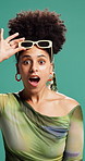 Face, woman and surprise with sunglasses in studio for fashion sale, discount deal or promo offer. Trendy outfit, african person and omg reaction to bargain or retail announcement on green background